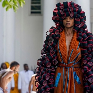 This time, the weather gods were smiling on Kerby Jean-Raymond and his label, Pyer Moss. So too were the fashion gods. Two days after torrential rains and lightning sent guests fleeing for cover and forced Jean-Raymond to postpone unveiling his hotly awaited first couture collection, the sun came out Saturday and the crowds came back. They were rewarded with a hugely imaginative, visually audacious show that blurred the lines between fashion and art as it paid tribute to the ingenuity of Black inventors often overlooked by history. And so, there was the peanut butter dress — literally, a huge, soft sculpted jar of the stuff. There was a stunning hot roller cape — which was what it sounds like, hot rollers from head to toe. There was an ice cream cone with chaps for the cone. There was an air-conditioning unit, an old-fashioned mobile phone, a kitchen mop. There was a pastel pink lampshade dress, with beaded fringes. There was a chess board, and a white metal folding chair, and a bottlecap — each costume a sophisticated work of sculpture. There was also a refrigerator with colorful letter magnets spelling out the phrase: "But who invented Black trauma?" There were also dancers, a rap musician, a string section, and a history lesson from Elaine Brown — activist, writer and a former leader in the Black Panther Party. Jean-Raymond, whose shows always entwine his ideas about fashion with those about culture, race and society, said in an interview after the show that his goal was "to highlight inventions by Black people and show them in a nontraditional way," involving 3D construction and sculpture. Tap link in bio to continue on @EDGEmedianetwork ???️‍? (?: Pyer Moss / AP / Bebeto Matthews)