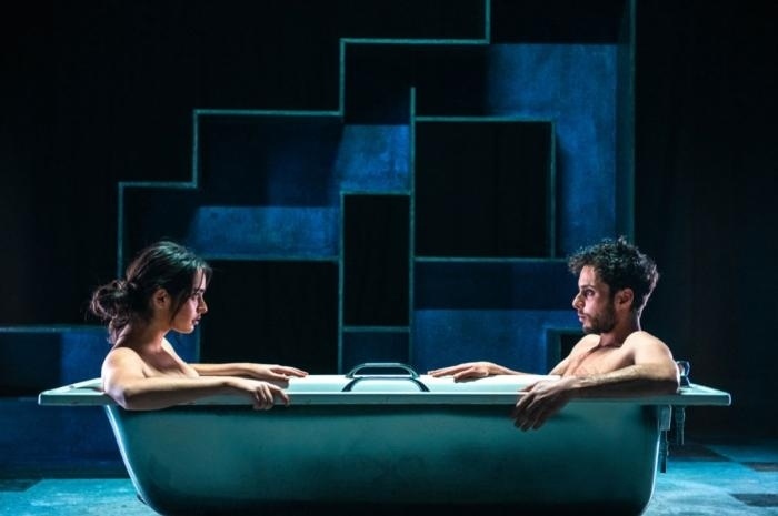 "Adam," an hourlong play written by Frances Poet, stars Adam Kashmiri and is based on Kashmiri's experiences as a transgender man, first in his native Egypt — where he faces constant misgendering and dangerous anti-LGBTQ+ sentiment — and then as a refugee seeking asylum on Scotland. "Adam" pushes buttons that not even the acclaimed documentary "Flee," also about an LGBTQ+ refugee from an Arabic country, put its finger on. The story is told, adroitly and with emotional force, through a mixture of flashbacks and present-day interactions with a mental health nurse (Stephen McCole) who's come to check on Adam — who, at that point, has been living in isolation for 403 days (a tally that grows to 600 as his struggle continues). Not much about this play is gentle, in fact, but everything about it speaks to the needless pain and terror transgender people are subjected to in repressive places around the world — which, sadly, includes a number of American states. The pay's universality and unflinching honesty give it a harrowing power, but also a deeply affecting poignance that's amplified, and given voice anew, by a choir of 140 transgender and non-binary singers from around the world.  A haunting work, "Adam" holds out hope for healing and happiness. It's a story that needs to be told — now more than ever. Streaming this week @artsemerson ⁠
⁠
Tap link in bio to continue on @EDGEmedianetwork⁠
?️‍??️?️⁠
?️: Kilian Melloy / @dragelruairi ⁠
?: Yasmin Al-Khoudhairi and Adam Kashmiri in 'Adam'  / National Theatre Of Scotland @ntsonline