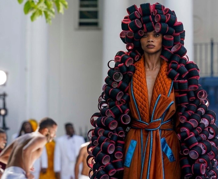 This time, the weather gods were smiling on Kerby Jean-Raymond and his label, Pyer Moss. So too were the fashion gods. Two days after torrential rains and lightning sent guests fleeing for cover and forced Jean-Raymond to postpone unveiling his hotly awaited first couture collection, the sun came out Saturday and the crowds came back. They were rewarded with a hugely imaginative, visually audacious show that blurred the lines between fashion and art as it paid tribute to the ingenuity of Black inventors often overlooked by history. And so, there was the peanut butter dress — literally, a huge, soft sculpted jar of the stuff. There was a stunning hot roller cape — which was what it sounds like, hot rollers from head to toe. There was an ice cream cone with chaps for the cone. There was an air-conditioning unit, an old-fashioned mobile phone, a kitchen mop. There was a pastel pink lampshade dress, with beaded fringes. There was a chess board, and a white metal folding chair, and a bottlecap — each costume a sophisticated work of sculpture. There was also a refrigerator with colorful letter magnets spelling out the phrase: "But who invented Black trauma?" There were also dancers, a rap musician, a string section, and a history lesson from Elaine Brown — activist, writer and a former leader in the Black Panther Party. Jean-Raymond, whose shows always entwine his ideas about fashion with those about culture, race and society, said in an interview after the show that his goal was "to highlight inventions by Black people and show them in a nontraditional way," involving 3D construction and sculpture. Tap link in bio to continue on @EDGEmedianetwork ???️‍? (?: Pyer Moss / AP / Bebeto Matthews)